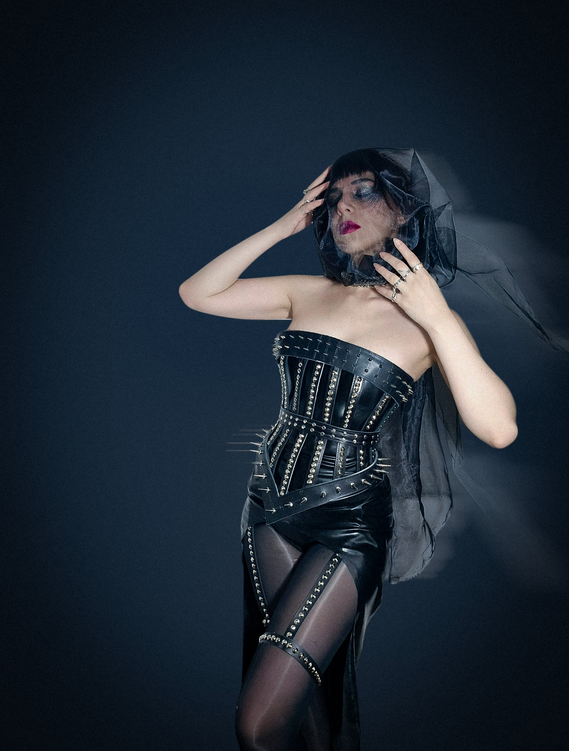 black leather cage corset with spikes, layered latex shorts, Latex top and a latex skirt, a spiked leather harness, and a hand-woven metal choker.
